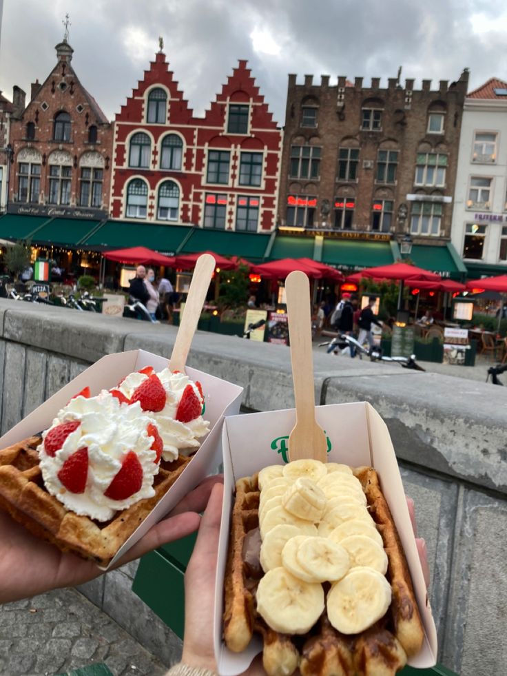 two waffles with bananas, strawberries and whipped cream on them in front of some buildings