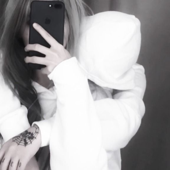 a woman in white hoodie taking a selfie with her cell phone while wearing an earring