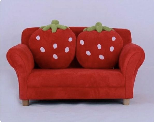 a red couch with two strawberry pillows on it's back and the seat up