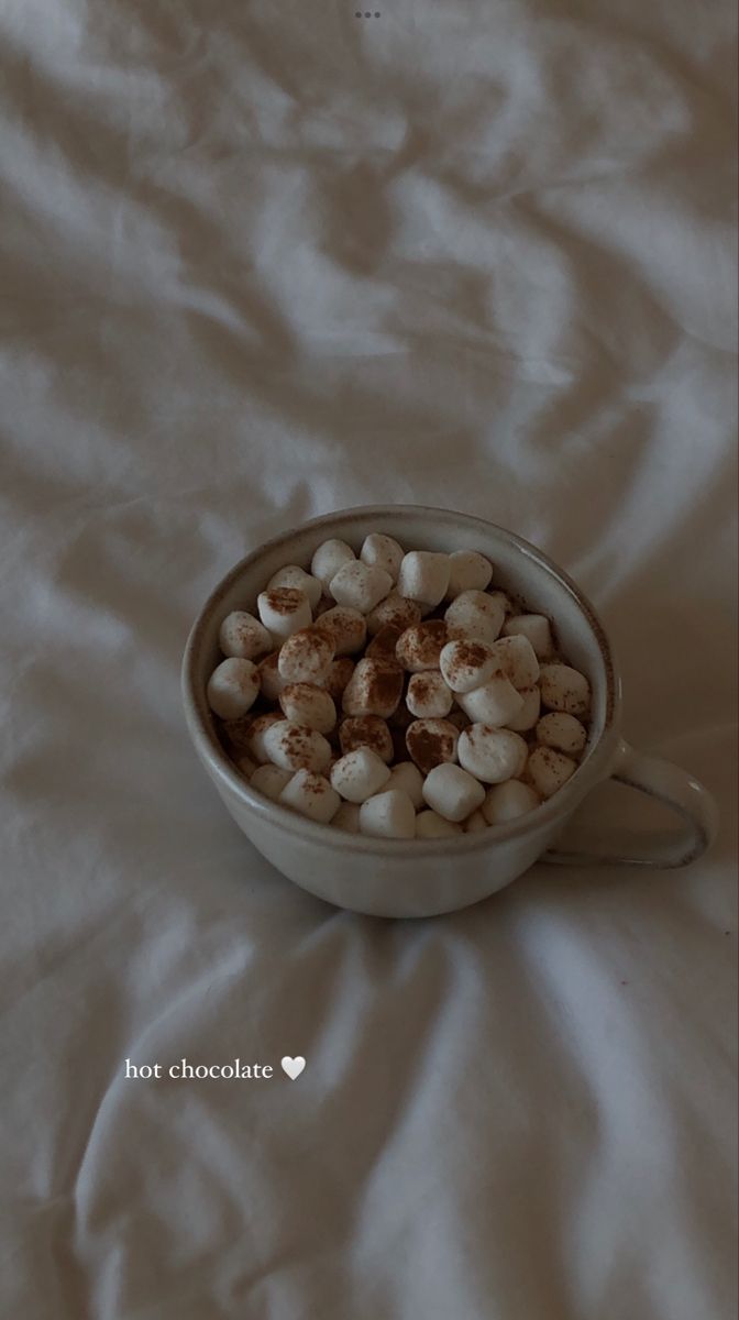 a bowl filled with marshmallows sitting on top of a white bed sheet