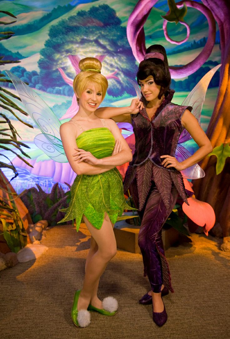 two women dressed as tinkerbells in front of a backdrop with trees and plants