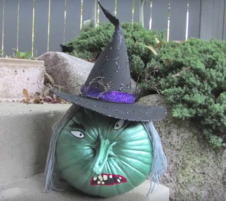 a green pumpkin with a witch hat on it's head sitting in front of some bushes