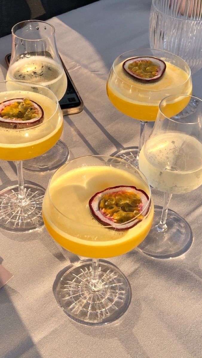 four glasses filled with different types of drinks on a table cloth covered tablecloth, next to two empty wine glasses and a cell phone