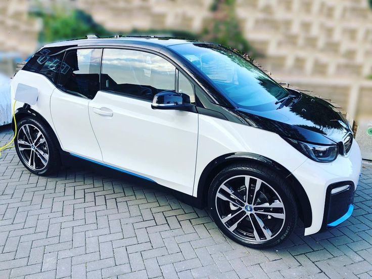 the bmw i3 electric car is parked in front of a brick wall and sidewalk