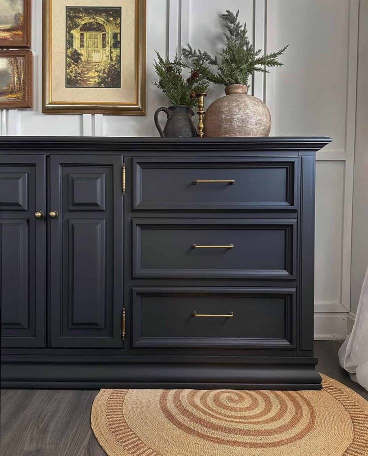 a black dresser with gold handles and drawers in a white room next to pictures on the wall