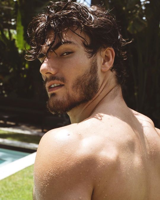 a man with no shirt standing in front of a pool and looking off into the distance