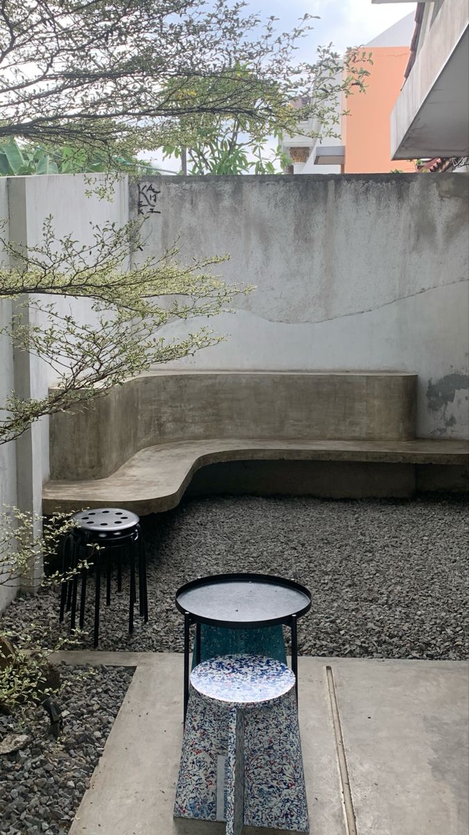 an outdoor seating area with tables and stools on the ground in front of a concrete wall