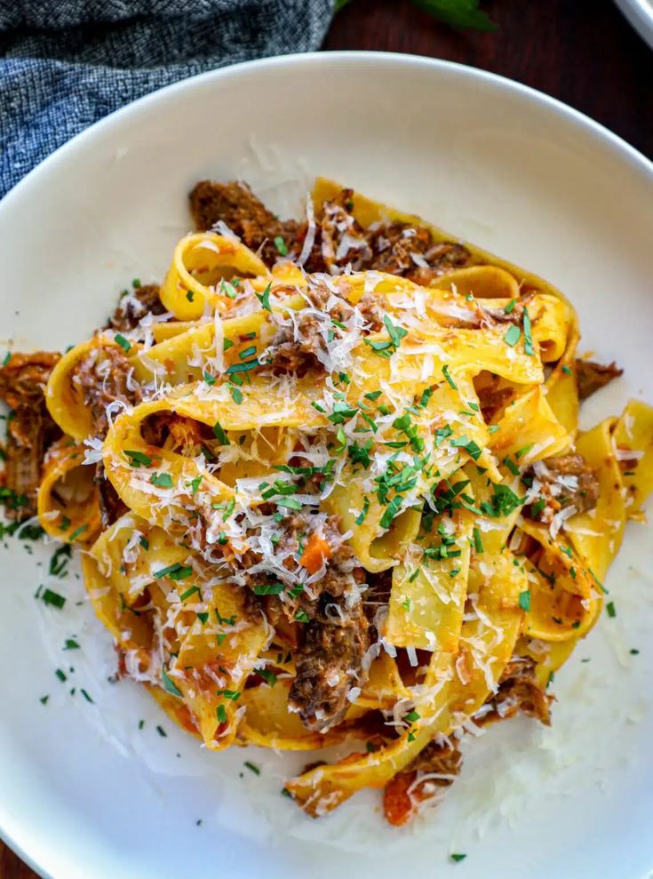 a white plate topped with pasta and meat covered in sauce, parmesan cheese