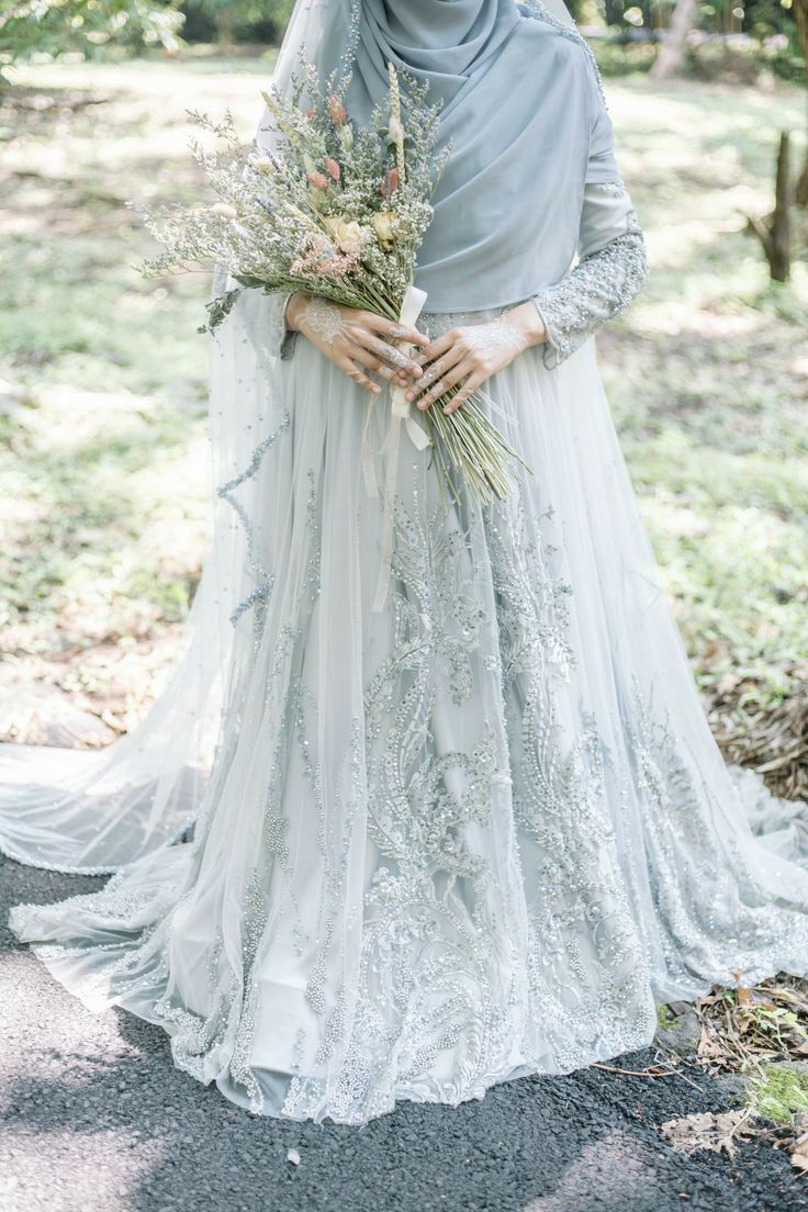 a woman in a wedding dress holding flowers and standing on the side of a road