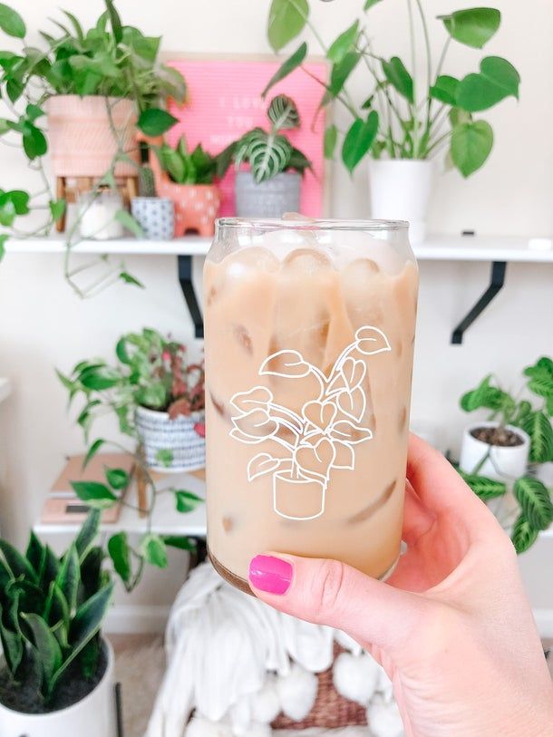 a person holding up a drink in front of some potted plants