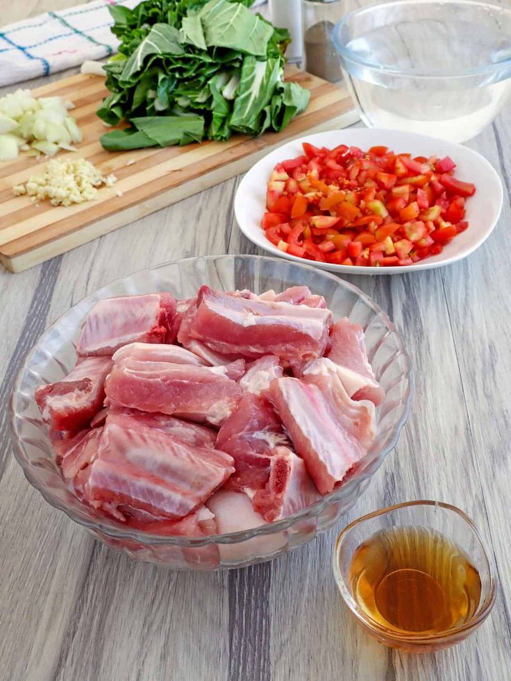 chopped meat and vegetables on a table next to a glass bowl with olive oil in it