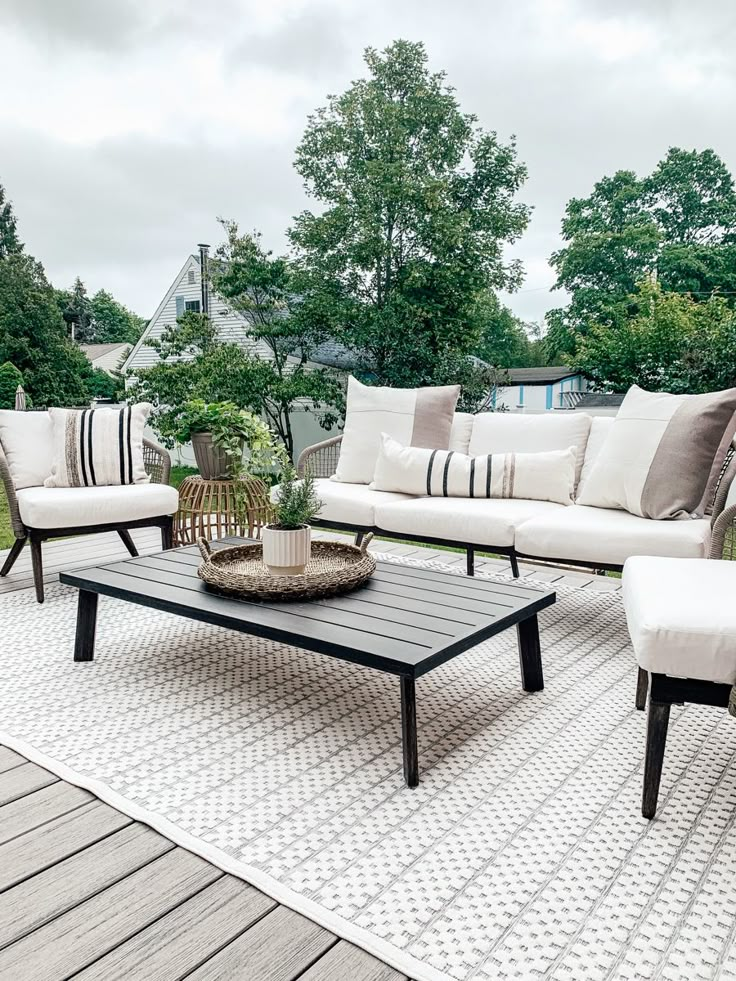 a couch and table sitting on top of a wooden deck next to a tree filled yard