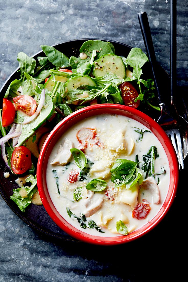 a red bowl filled with soup next to a salad on top of a black plate