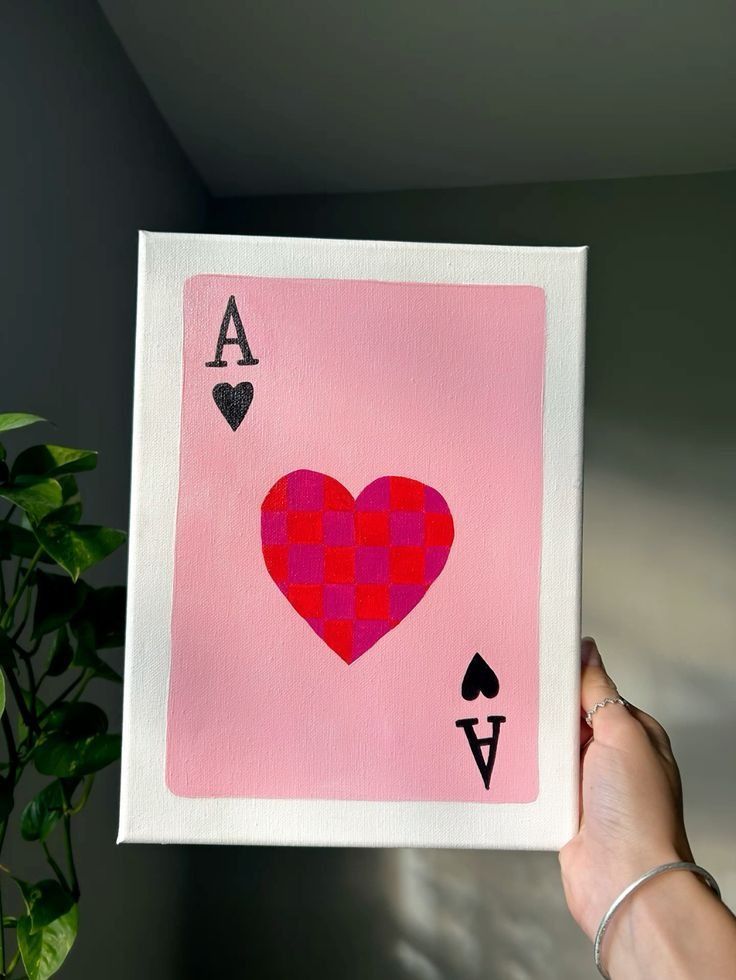 a hand holding up a pink playing card with hearts and spades on the back