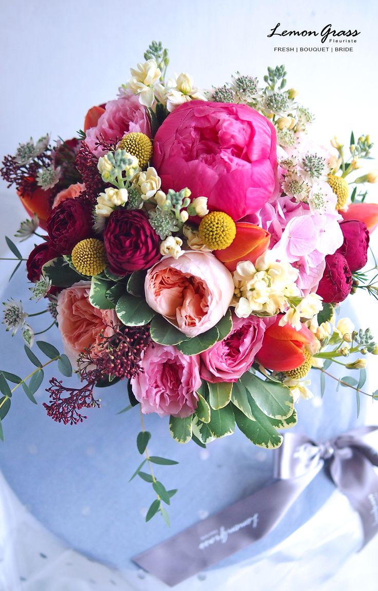 a bouquet of flowers is sitting in a blue vase on a white surface with a ribbon tied around it