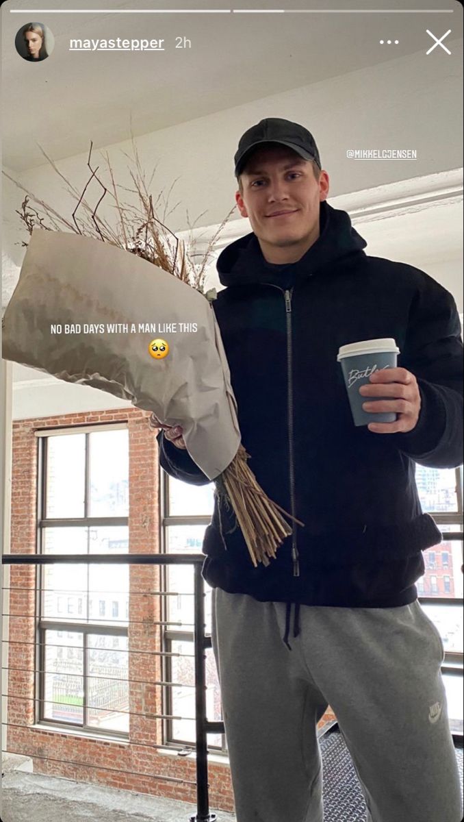 a man holding a coffee cup and a fake plant in his hand while standing next to a window