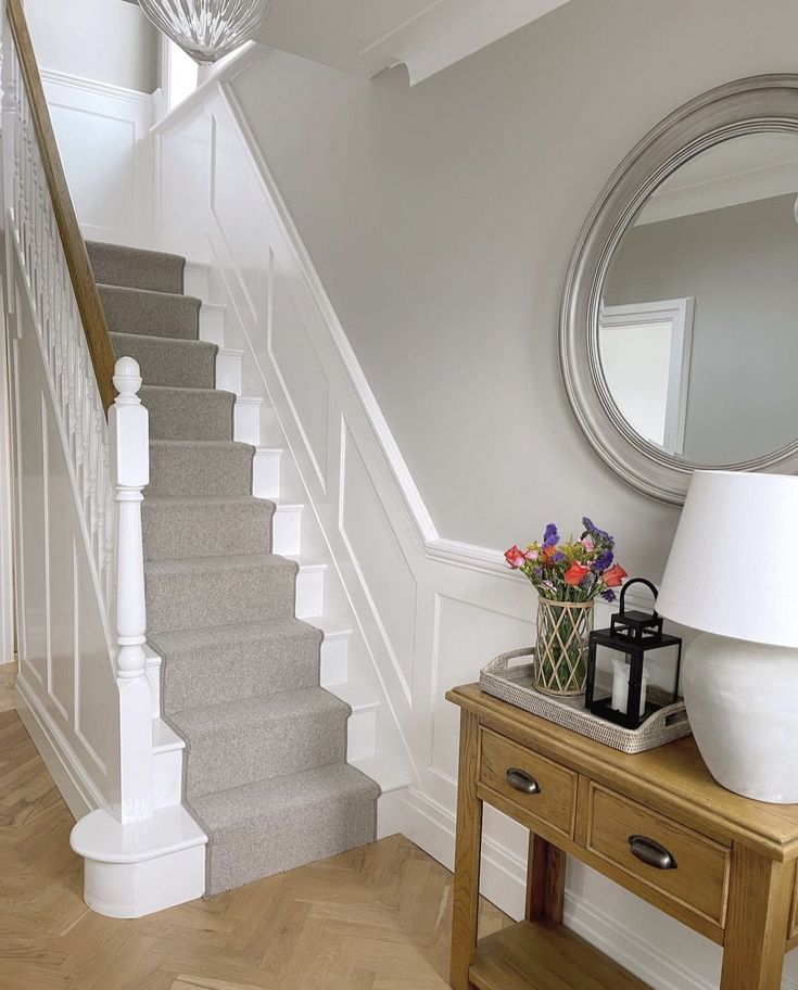 there is a vase with flowers sitting on the table next to the stair case and mirror