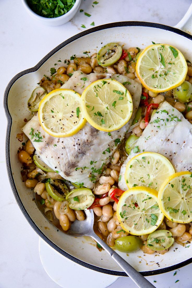 fish with lemons, beans and vegetables in a skillet