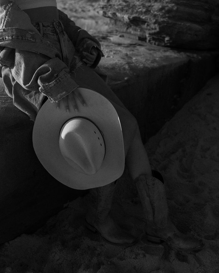 a person sitting in the sand with a cowboy hat on their head and one leg up