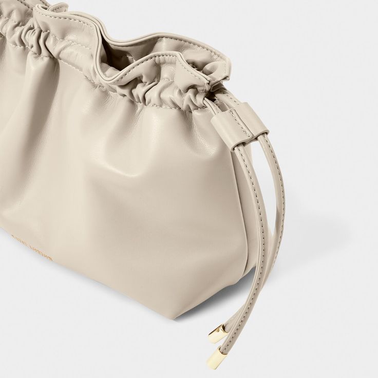 Discover the latest addition to the Katie Loxton family - the Hailey Crossbody Clutch in greige! This versatile bag offers you two stylish ways to wear it - either as a trendy crossbody for an effortless day look or as an elegant clutch to elevate any evening outfit. With its drawstring closure detail, vegan leather material, and gleaming gold-tone hardware, this bag exudes understated luxury and attention to detail. Sure to become a staple in your wardrobe, and a piece you can rely on for years Versatile Cream Pouch Shoulder Bag, Versatile Cream Pouch Bag, Chic Neutral Shoulder Bag With Adjustable Strap, Chic Cream Shoulder Bag For Travel, Neutral Crossbody Shoulder Bag With Removable Pouch, Chic Neutral Shoulder Bag With Removable Pouch, Chic Neutral Satchel Shoulder Bag, Feminine Cream Bags With Removable Pouch, Modern Cream Shoulder Bag For Spring