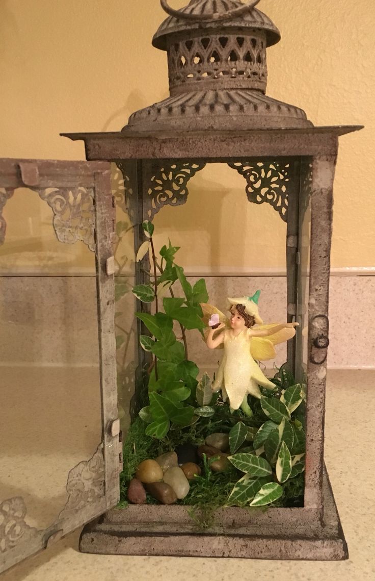 a fairy figurine in a lantern with plants and rocks