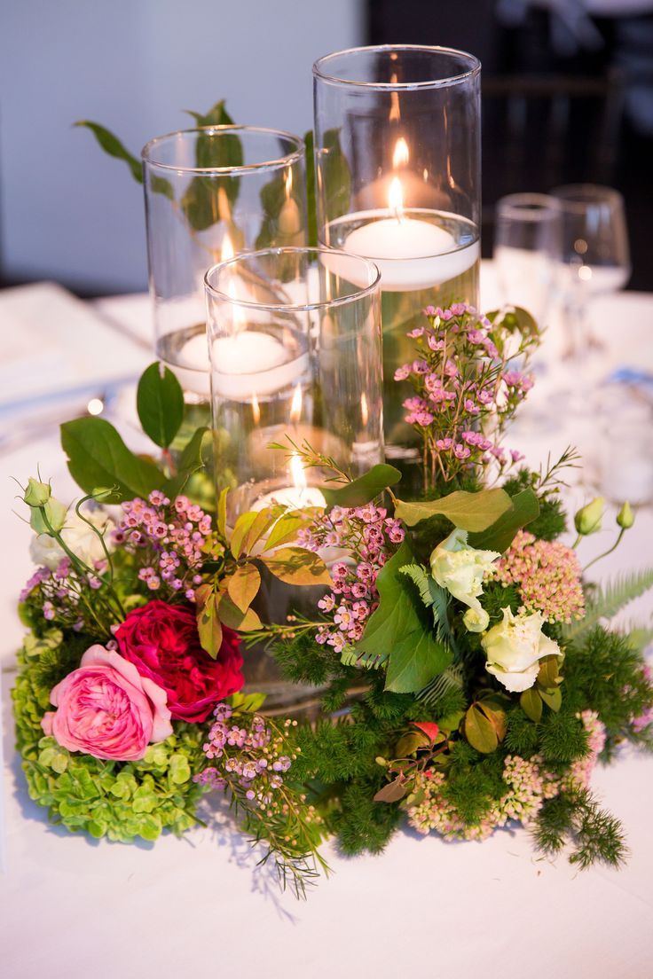 flowers and candles are arranged on a table with white linens, greenery and glass vases