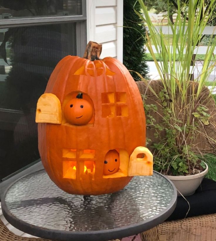 a pumpkin with faces carved into it sitting on top of a metal table in front of a house