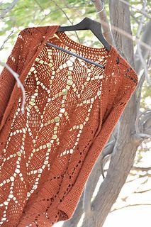 an orange crocheted sweater hanging from a tree