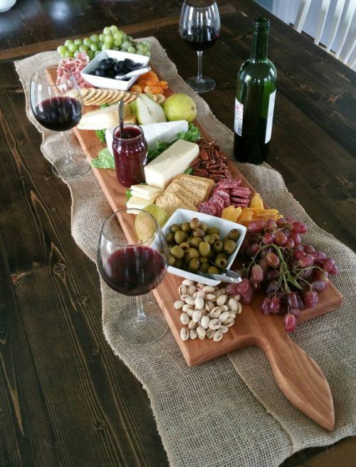 a wooden tray topped with lots of different types of food next to a glass of wine