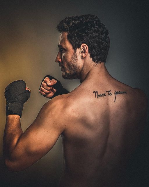 a man with a tattoo on his back holding a boxing glove and looking at the camera