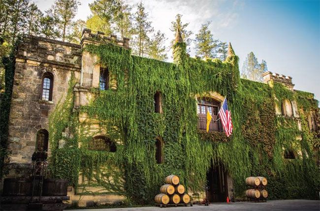 an old building with vines growing on it's side and wine barrels in front