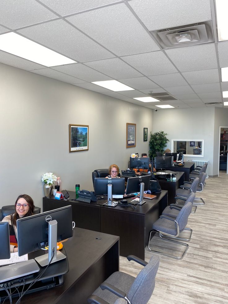 two women sitting at desks in an office setting with computers on each side of the desk