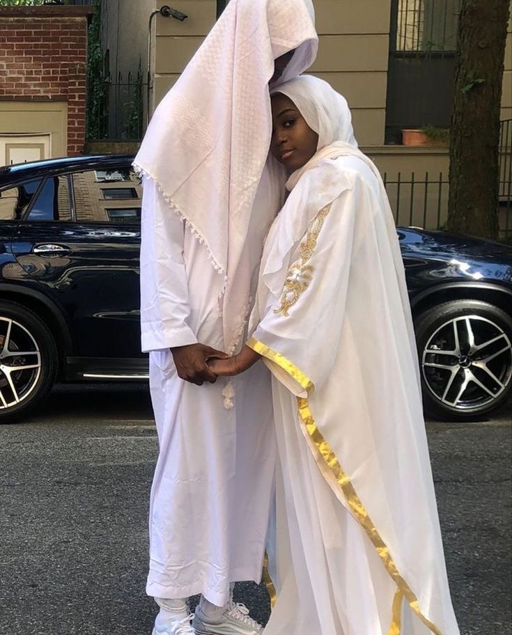 two people dressed in white standing next to each other on the street with cars behind them