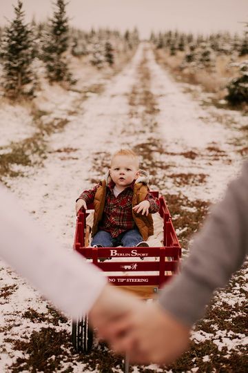 a young boy sitting in a red wagon on top of snow covered ground