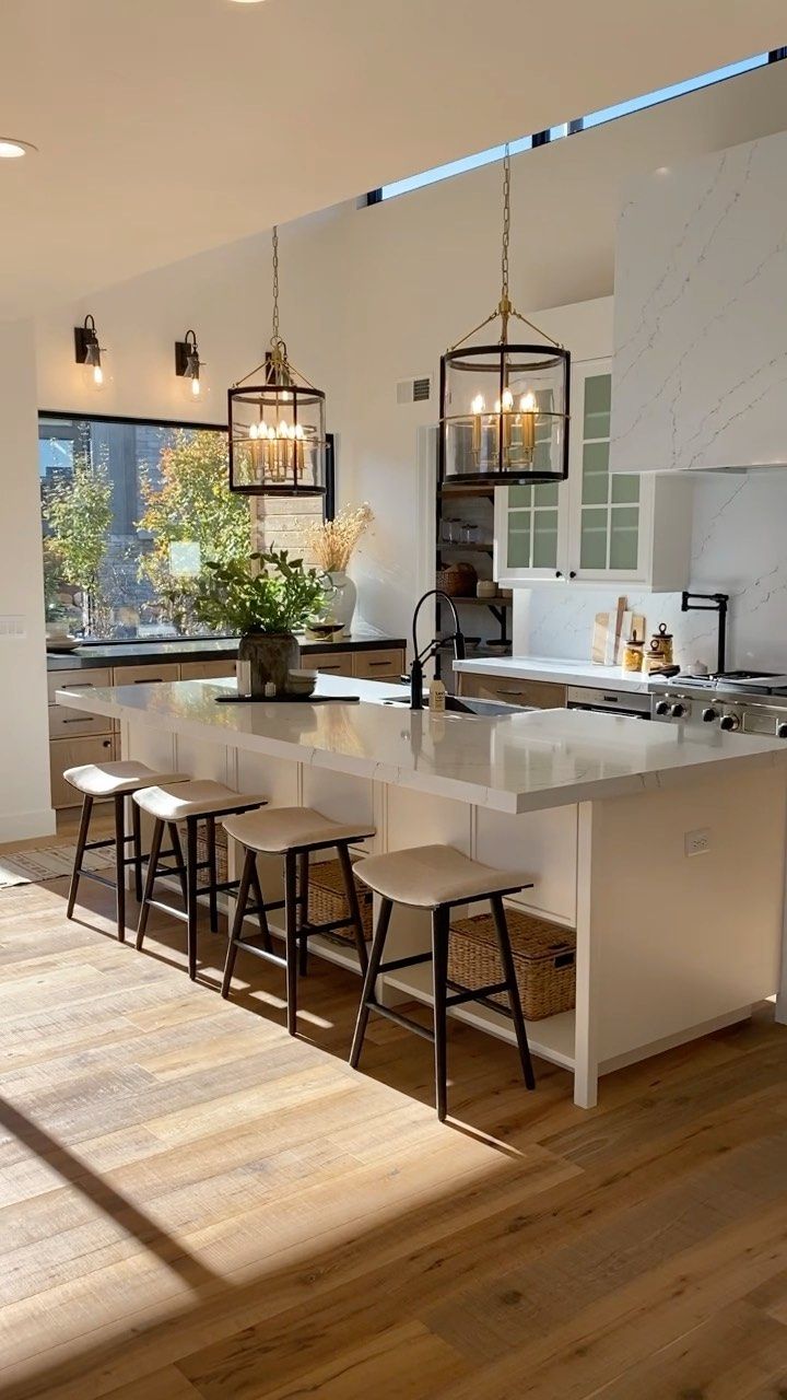 a kitchen with an island and chairs in the center, lights hanging from the ceiling