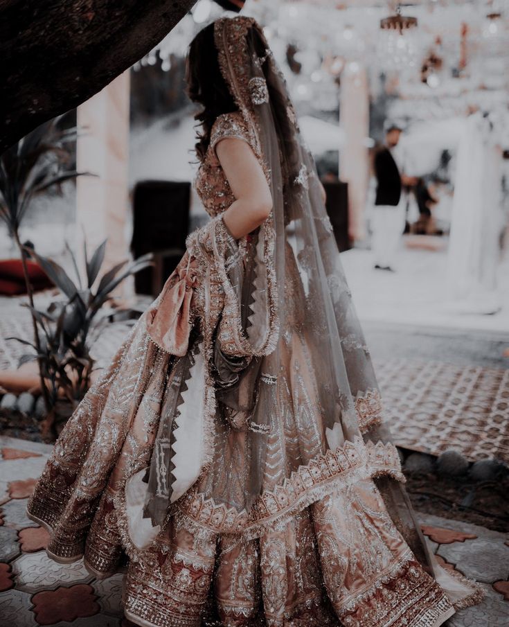 a woman in a bridal gown and veil standing under a tree with her back to the camera