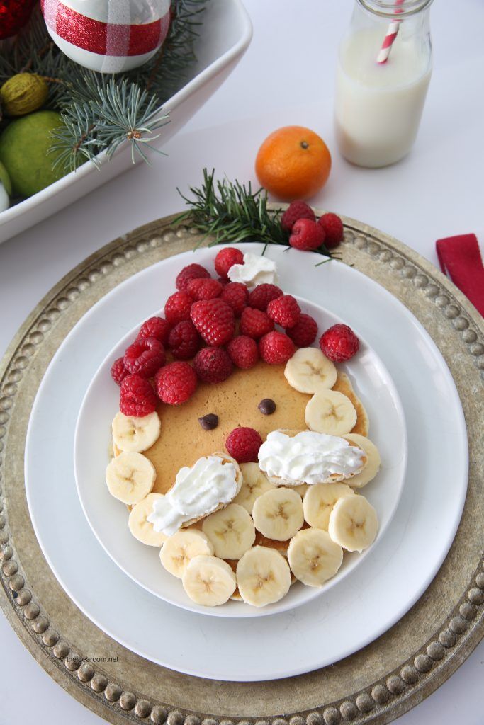 a white plate topped with pancakes covered in bananas and raspberries next to oranges