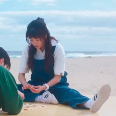 three people sitting on the sand at the beach and one person is touching her hands