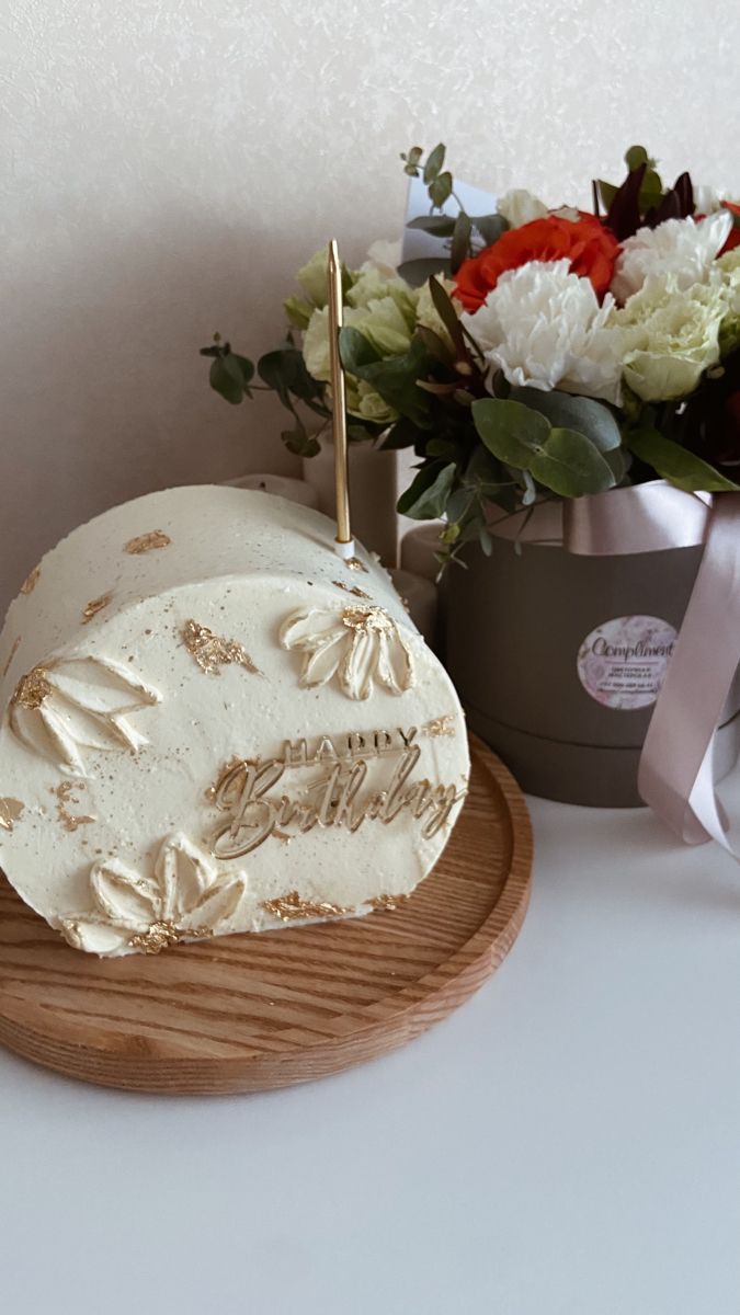 a white cake sitting on top of a wooden plate next to a vase with flowers