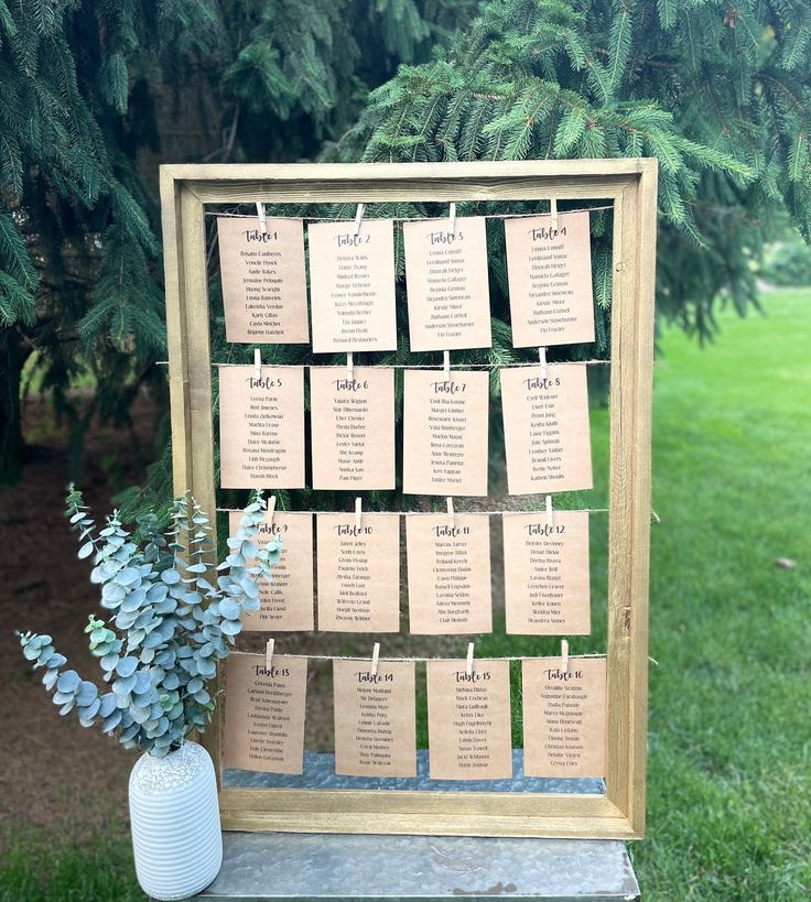 a wooden frame with seating cards attached to it next to a vase filled with flowers