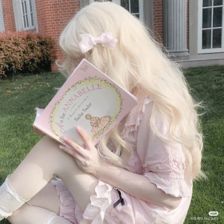 a woman sitting on the grass with a book in her hand and holding it up to her face