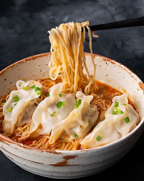 a bowl filled with noodles and sauce being held by a pair of chopsticks