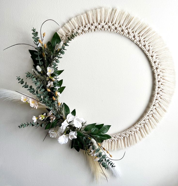 a wreath made out of yarn with flowers and feathers on the front, along with greenery