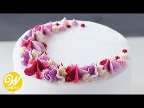 a white cake with pink and purple flowers on it's side, sitting on top of a table