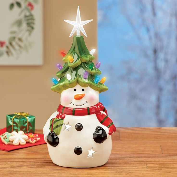 a ceramic snowman with a christmas tree hat and scarf around its neck on a table