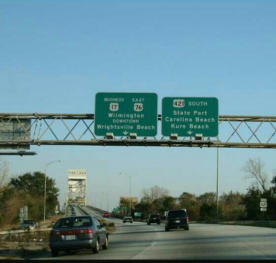 two green highway signs above a freeway with cars driving down the road in front of them