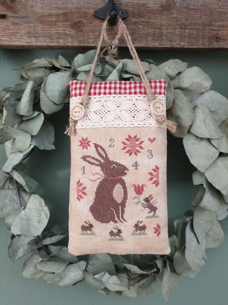 a wreath hanging on the wall with a cross - stitched bag attached to it