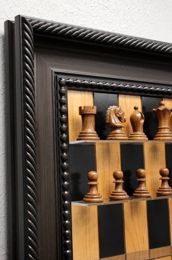 a wooden chess set in a black frame on the wall next to a white wall