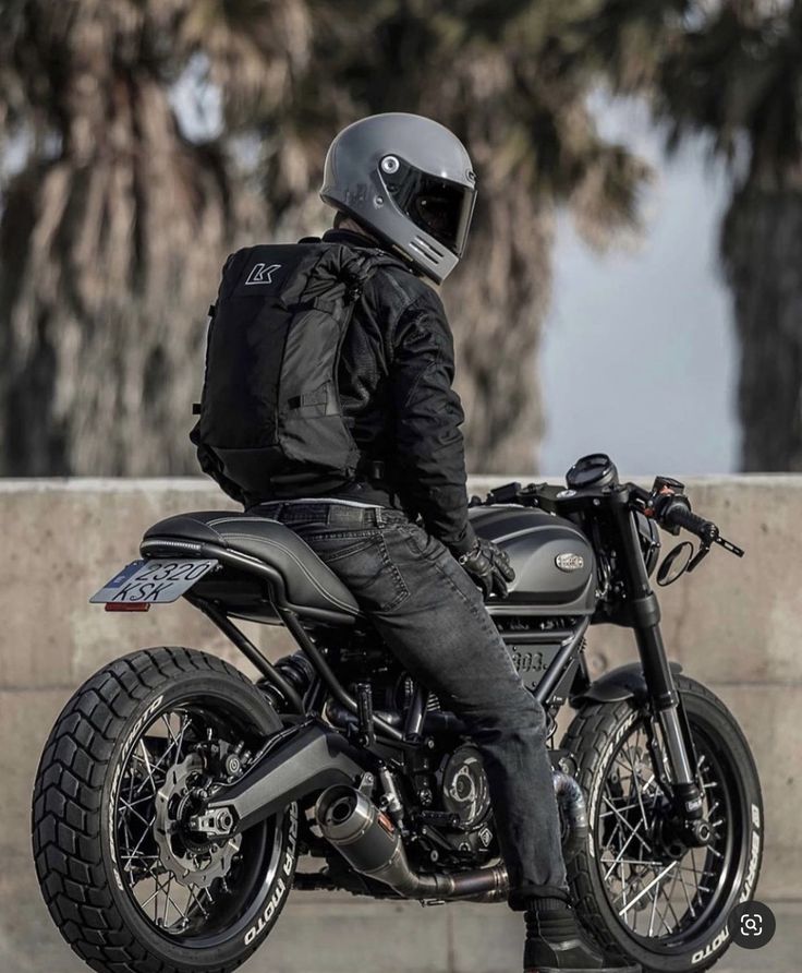 a man sitting on top of a motorcycle wearing a helmet and black jeans with his legs crossed