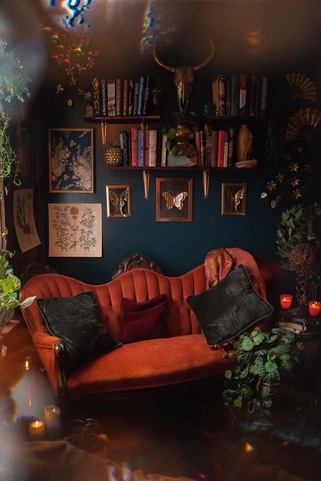 a living room filled with furniture and lots of books on the shelves above it is a red couch surrounded by plants